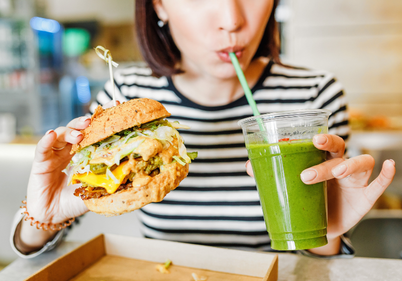 Frau trinkt grünen Smoothie und isst veganen Burger